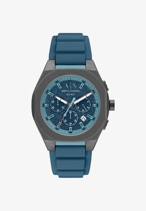 Hodinky s modrým silikonovým řemínkem, texturovaným modrým ciferníkem, stříbrnými detaily, chronografovými subciferníky a zobrazením data na pozici 6 hodin. Osmihranné pouzdro.