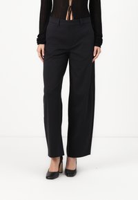 Black wide-leg trousers with a smooth texture, featuring a flat front, belt loops, and pockets. Worn with black high-heeled shoes.