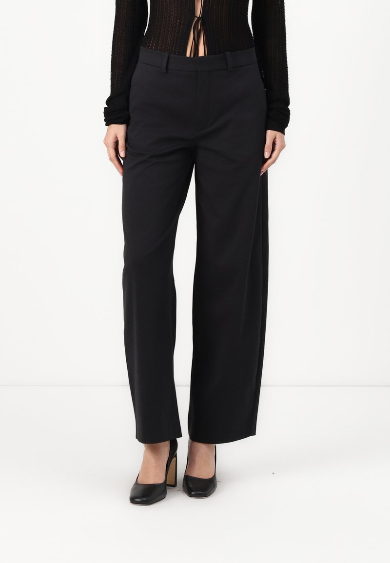 Black wide-leg trousers with a smooth texture, featuring a flat front, belt loops, and pockets. Worn with black high-heeled shoes.