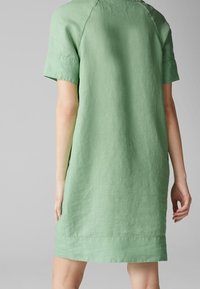 Grünes Leinenkleid mit kurzen Ärmeln und lässiger Passform, versehen mit einem runden Ausschnitt und einem schlichten Saum. Texturiertes Material mit minimaler Verzierung.