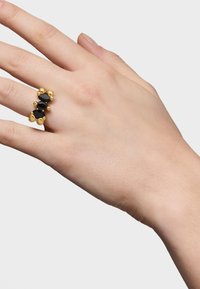 Anillo de oro con tres piedras ovaladas negras, acentuado con cuentas de oro redondeadas. El anillo tiene una textura suave y un diseño geométrico.
