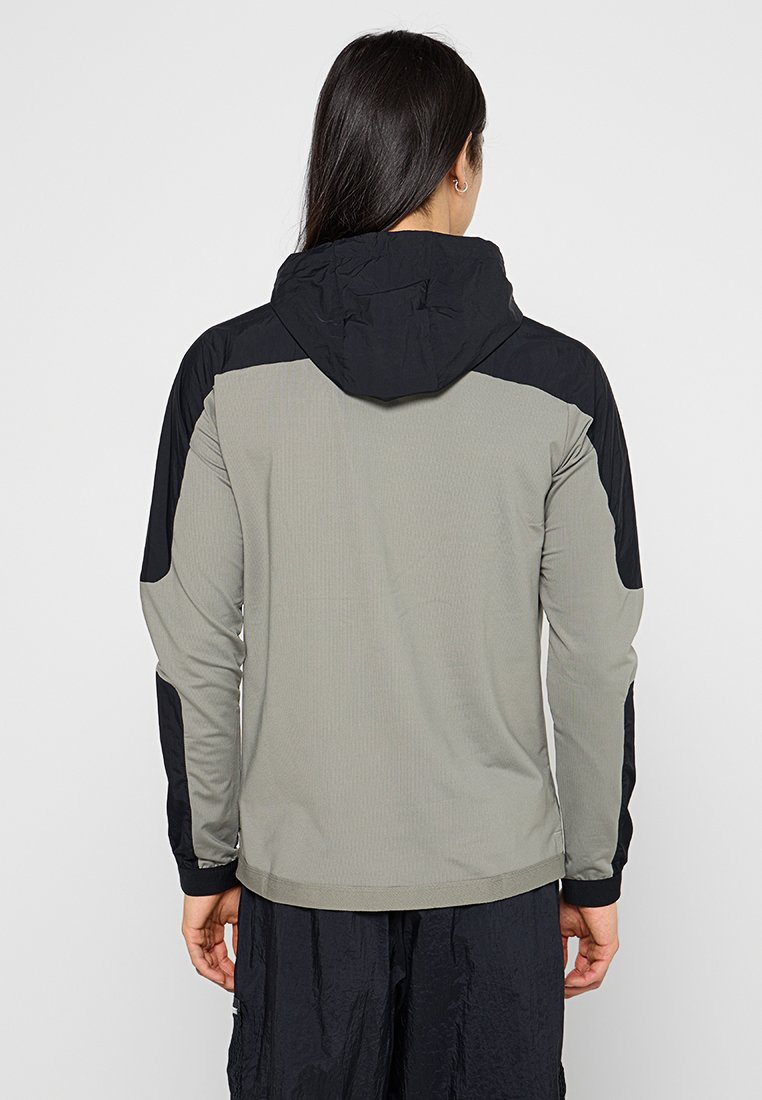 Veste à capuche présentant un corps gris avec des manches noires, un tissu texturé et un design épuré pour un ajustement moderne.