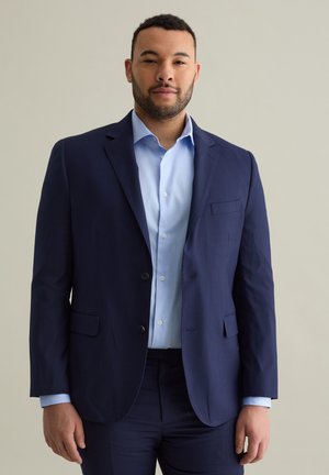 Navy blue suit jacket with a textured finish, two buttons, notched lapels, and a chest pocket, paired with a light blue dress shirt.