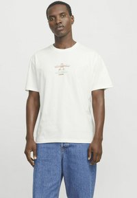 Creme kortærmet t-shirt lavet af bomuld. Har et trykt design med "Sandwich Deli" i orange og grøn. Klassisk pasform, rund halsudskæring.