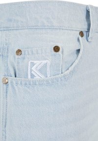 Light blue denim shorts with a textured finish, featuring a white stitched logo on the back pocket and bronze metal hardware accents.
