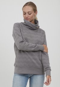 Šedá mikina s vysokým límcem, detaily s knoflíky a vzorem ve tvaru cik-cak. Dlouhé rukávy a volný střih. Materiál z bavlněné směsi.