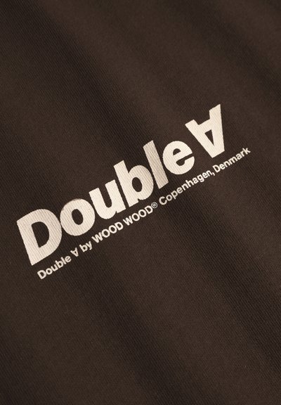 Texte blanc "Double A par WOOD WOOD Copenhague, Danemark" imprimé sur un tissu marron foncé.