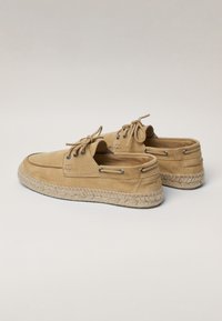 Hellbraune Wildlederschuhe im Bootsstil mit einer gewebten Jutesohle, ausgestattet mit Schnürungen und Metallösen für einen sicheren Sitz. Sanfte Textur und niedriges Profil-Design.