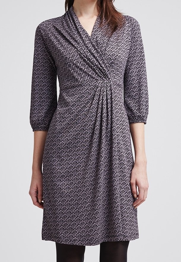 Femme portant une robe mi-longue à manches trois-quarts avec un motif géométrique violet et noir et un détail froncé à la taille.