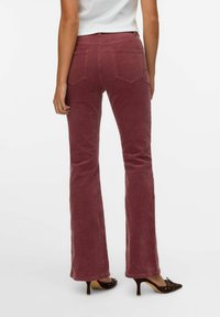 Pantalones de pana acampanados en un profundo tono rosa con una textura acanalada. Cuentan con dos bolsillos traseros y una cintura ajustada, combinados con zapatos de tacón marrones.