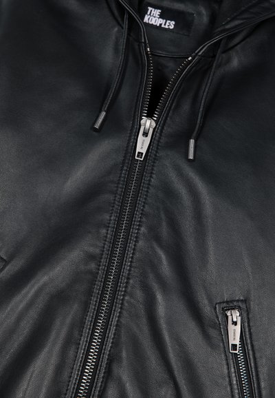 Zwarte leren jas met centrale zilveren rits, zijzak met rits en merketiket "THE KOOPLES" aan de binnenkant van de kraag.