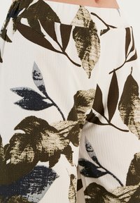 Bloemenprintstof met abstracte bladvormen in groen, marineblauw en crème. Lichte, gestructureerde stof met een elastische tailleband.
