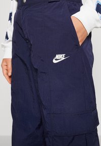 Marine nylon cargobroek met een soepele textuur, voorzien van een wit Nike-logo op de zak en een zijzak voor gereedschap.