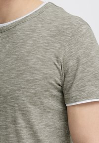 Tricou scurt cu mâneci scurte, de culoare verde măsliniu, cu guler alb, având un material moale și texturat și dungi orizontale subtile.