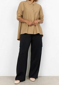 Light brown button-up shirt with short sleeves and a curved hem, paired with black wide-leg cargo pants featuring side pockets.