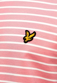 Ύφασμα με ροζ και λευκές ρίγες, που φέρει ένα κεντητό λογότυπο πουλιού σε μαύρο και κίτρινο, τοποθετημένο στη αριστερή πλευρά.