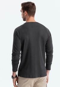 Tumma harmaa pitkähihainen paita, jossa on ribattu rakenne ja pyöreä kaula-aukko, raglanhihoilla ja yksinkertaisella takasuunnittelulla.