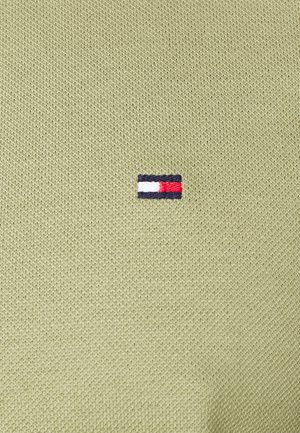 Małe prostokątne logo z poziomymi paskami w kolorach granatowym, białym i czerwonym, wyszyte na jasnozielonej, teksturowanej tkaninie.