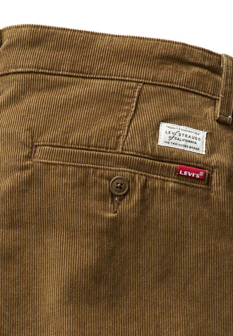 Tissu en velours côtelé marron avec des rayures verticales, comportant une fermeture à bouton, une poche arrière et une étiquette Levi's pour identifier la marque.