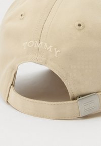Khaki kšiltovka s vyšitým textem "TOMMY". Má strukturovanou tkaninu, nastavitelné poutko a kovový akcent.