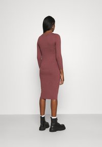 Ribbad klänning med långa ärmar i mauve, figursydd silhuett som slutar vid vaden, parat med svarta kängor och vita strumpor, visad från baksidan.