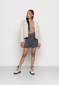 Jaqueta de cortiça bege com colarinho de fleece, suéter castanho cortado, saia de malha cinza e botas de combate creme com atacadores e solas pretas.