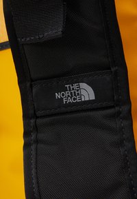 Black nylon strap with a textured finish, featuring a gray logo patch that reads "THE NORTH FACE" against a bright yellow background.