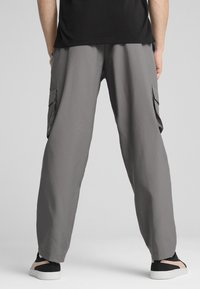 Light gray cargo pants made of soft fabric, featuring side pockets and a relaxed fit, paired with black and pink sneakers.