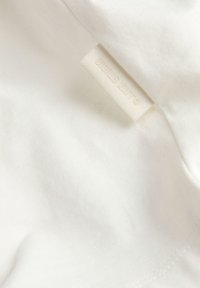 Λευκό ύφασμα με μια μικρή μπεζ ετικέτα ρούχου ραμμένη σε μια ραφή, με αχνό ανάγλυφο κείμενο.