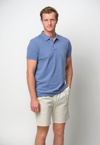 Ljusblå kortärmad pikétröja med krage, i kombination med beige shorts. Råkänsla, avslappnad passform och minimal detaljering.