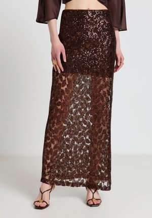 Langer brauner bestickter Rock mit transparenten floralen Spitzenpaneelen, getragen mit schwarzen Riemchenabsätzen, gezeigt von der Taille bis zu den Füßen.
