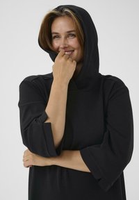 Czarny sweatshirt z kapturem, z rękawami do trzech czwartek, o miękkiej fakturze, luźnym kroju oraz małym wycięciem na rękawie.