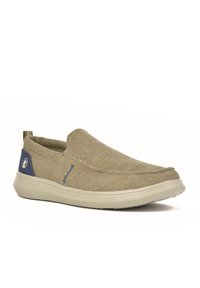 Zapatos tipo slip-on fabricados con tela beige de acabado texturizado. Presentan un acento en azul marino en el talón y una suela de goma ligera.