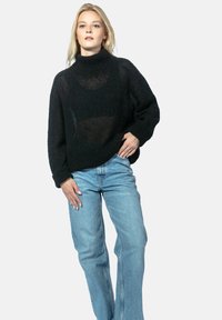 Czarny, dziany sweter z golfem o luźnym kroju i prążkowanymi mankietami, w połączeniu z jasnoniebieskimi, jeansami z wysokim stanem. Miękka, lekko przezroczysta faktura.