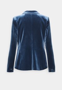Veste en velours bleu profond avec une coupe ajustée, un revers cranté, des manches longues et des détails subtils en argent sur les poignets. Texture lisse.