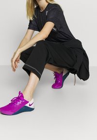 Czarny t-shirt sportowy z teksturowanej tkaniny, w połączeniu z luźnymi czarnymi spodniami 3/4. Jasnoróżowe i niebieskie sneakersy z wiązaniem.