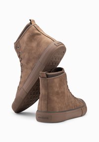 Zapatillas altas marrones de ante, con una suela de goma texturizada, diseño de cordones y un detalle del logo en el talón.