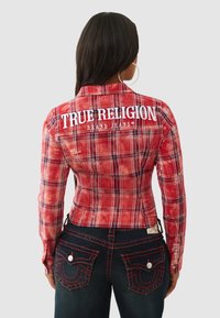 Czerwona koszula w kratę o dopasowanym kroju z długimi rękawami i logo. Zestawiona z ciemnymi dżinsami ozdobionymi czerwonym przeszyciem i kieszeniami.