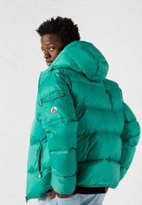 Giacca a vento turchese con cappuccio, dotata di tasca con zip sul maniche e di una patch con logo. Realizzata in materiale lucido e trapuntato.