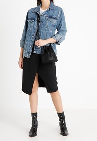 Kurtka dżinsowa w jasnoniebieskim kolorze, z zapięciem na guziki i dwoma przednimi kieszeniami. Czarna spódnica z rozcięciem na udzie. Błyszczące czarne botki za kostkę. Czarna torebka o fakturze.