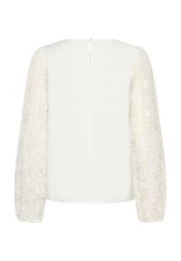 Blouse blanche avec manches longues en dentelle transparente, encolure arrondie et fermeture éclair au centre du dos. Tissu lisse sur le corps avec un motif floral en dentelle.