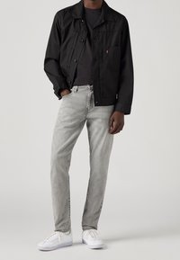 Czarna kurtka z płótna z zapięciem na guziki, szare dżinsy oraz białe trampki. Kurtka ma kieszeń na piersi i luźny krój.