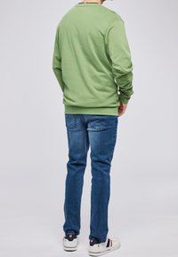 Vihreä pitkähihainen paita pyöreällä pääntiellä, yhdistettynä sinisiin farkkuihin ja valkoisiin lenkkareihin, joissa on punaisia ja laivastonsinisiä yksityiskohtia.