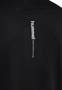 Zwarte shirt met textuur en een verticale witte logo met de tekst "hummel PERFORMANCE" op de achterkant. De stof lijkt ademend en lichtgewicht te zijn.