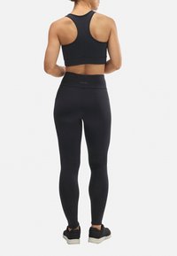 Sujeción deportiva negra sin costuras y leggings de cintura alta, ambos fabricados con material elástico. Diseño de espalda nadadora en la parte superior, textura suave en general.