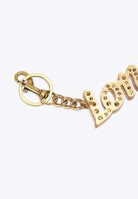 Złoty brelok z napisem "love" z podniesionymi literami ozdobionymi przezroczystymi cyrkoniami, połączony metalowym łańcuszkiem i zapięciem.