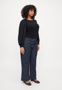 Black top with textured sparkly bodice and long puff sleeves, paired with wide-leg dark blue denim jeans, and black patterned flats.