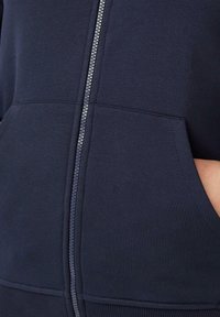 Marineblauwe zip-up hoodie met een zilveren rits, voorzien van kengOeroe-zakken en ribgebreide manchetten. Zacht, textuurachtig materiaal met een casual ontwerp.