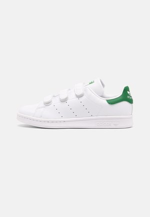 Witte Adidas Stan Smith sneaker met groene hielkap, drie klittenbandsluitingen, geperforeerde zijstrepen en een platte zool.
