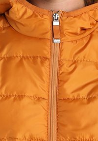 Orange pufferjacka med dragkedja fram, huva och en quiltad yta. Tyget har en slät, glänsande finish.